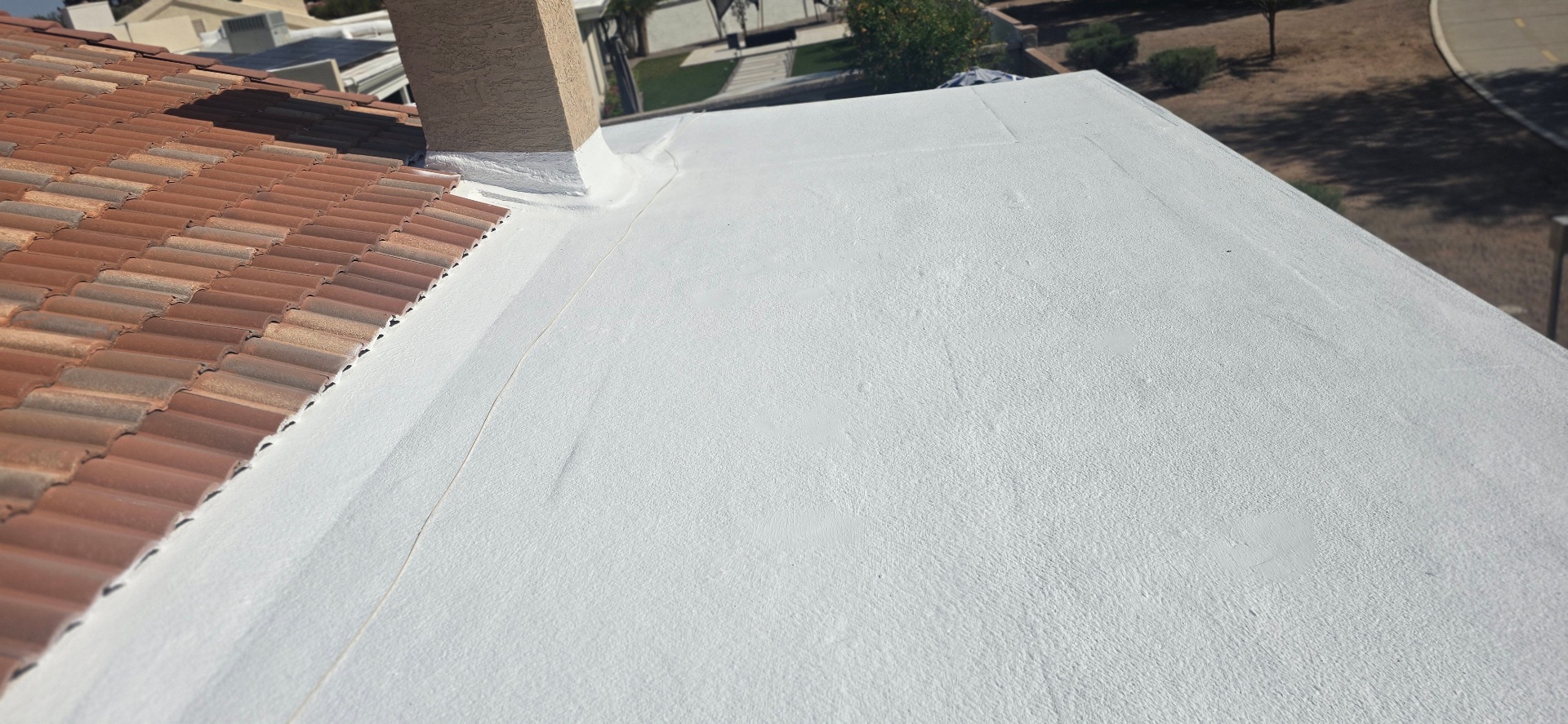 Tile-to-flat transition recoat · Phoenix Valley — Failing coating on a low-slope section that ties into a concrete-tile roof — chronic leaks at the chimney and the tile-to-flat transition.
